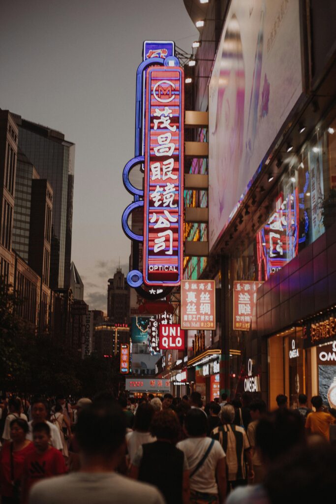 Bustling night scene in Shanghai with neon signs and crowds shopping under illuminated buildings.
